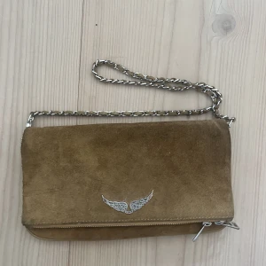 Zadig axelväska - Säljer en Zadig axelväska i en beige/brun färg med Zadig loggan på framsidan. Den är perfekt o ta med om man ska t stan elr bara ha med i handen🙌🏽🙌🏽  bandet tillkommer fast till väskan o är en kedja vävd med mocka likande material🤍🤍 