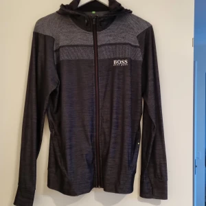 Hugo boss hoodie - Svart grå med röda detaljer. Fint skick. Dragkedja i fickorna. Tunt material. Slim fit. Fint skick.