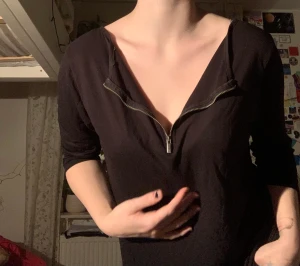 Svart tröja med dragkedja  - Svart tröja i mjukt tyg. Dragkedja som slutar nedanför nyckelbenet, går att ha kedjan både fram och bak. Ärmarna slutar i armvecket 