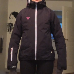 Tenson skidjacka - I princip oanvänd skidjacka från tenson, använd väldigt väldigt få gånger. Varmfodrad och i storlek 36. Dragkedjorna har reflex, med rosa detaljer. Jackan är väldigt mörkt blå, nästan svart. Jackan har en innerficka, liftkortsficka samt två vanliga.