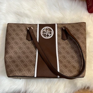 guess handväska  - superfin brun handväska från märket guess, knappt använd så i nyskick. mycket rymlig med många fack!
