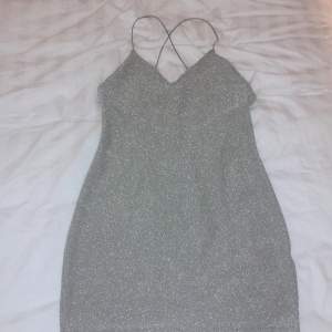 Glittrig grå rygglös klänning. Klänningen är använd en gång. Den är tunn och har spagetti straps som går i kors. Fintskick. Storlek S, men passar XS och M med. 