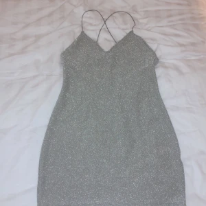 Glittrig Klänning. Storlek S - Glittrig grå rygglös klänning. Klänningen är använd en gång. Den är tunn och har spagetti straps som går i kors. Fintskick. Storlek S, men passar XS och M med. 