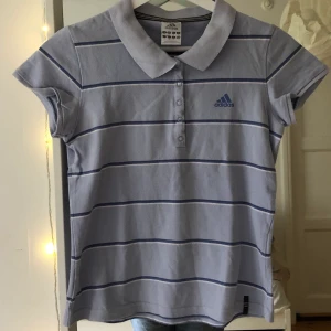Adidas piké  - En ljus lila/blå Adidas piké. Sitter väldigt snyggt med typ lågmidjade jeans. Skriv vid frågor eller för fler bilder!!