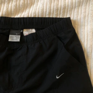 Low waisted Nike nylon byxor - Low waisted Vintage Nike byxor från 00-talet strlk XS. I väldigt fint skick utsvängda och går att justera med band nere vid ankeln. Har tyvärr en liten slitning vid ena benet, fråga för bild. 
