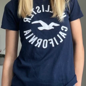 Marinblå t-shirt med tryck från hollister i strl xs - Marinblå t-shirt med tryck från Hollister i strl xs. Passar i storleken och superskön i  materialet. Köparen står för frakt!
