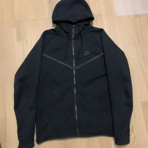 Nike tech fleece, svart - En svart Nike tech fleece i storlek herr M. Denna är en äldre tech fleece modell med snören till luvan och är därför svårare att få tag på. Skriv till mig för fitpic, mått eller annat! Kan fraktas eller mötas upp i Malmö/Lund.