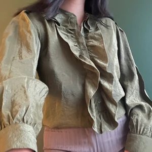 Kråsblus  - Olivgrön kråsblus i skimmrigt material. Bra skick. Knappar upptill/framtill men inte hela vägen ner. frakt ej inkl i priset. bra skick!