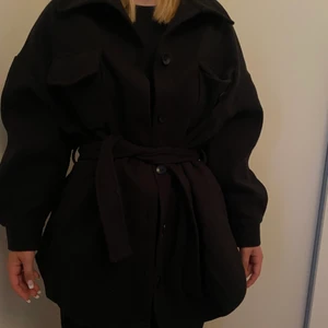 Svart kappa - En svart kappa med fina fickor vid brösten samt en fin knytdetalj runt midjan. Det finns även knappar längst hela jackan som ger möjlighet att stänga. Köpt från Boohoo, aldrig använd. Storlek 36, säljes för 200🧥
