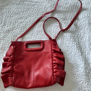 Röd väska - Maje  - En röd märkesväska från Maje, kan bäras på två olika sätt med det långa bandet och handtaget. Relativt sliten. Stängs med magnet. 