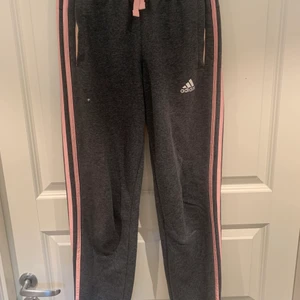 Mörkgrå adidas byxor  - Mörkgrå adidas byxor med rosa ränder på sidorna, det finns ett litet ”hål” de andra bilden, men annars bra skick 