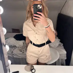 En beige playsuit med svart band vid midjan. Storlek 36 och playsuiten är helt oanvänd därav prislapp kvar. FRAKT 69kr