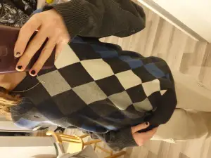 En långärmad tröja med blåa, gråa, svarta och vita rutor. Den har en lite v-ringning och är ribbad i slutet av ärmarna och längst ner på tröjan