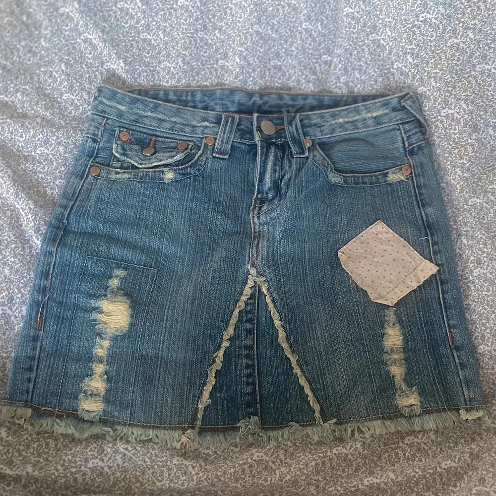 Jeanskjol från True Religion, gjord i USA. Den har många coola detaljer, som slitningar och blommiga patches. Det syns inte rikrigt på bilderna men den har småblommigt tyg under hålen också! Storleken är W29 (midjemått är dock 79 cm) men eftersom den är ganska rak i formen kan man välja lite hur högt man vill ha den, så kan tänka mig att den borde passa på S-M. . Kjolar.