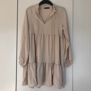 Klänning  - Fin lite oversize klänning, som är snygg till  boots. Fägen är för ljus för mig därför jag ej behåller den. Färgen är mer ljusbeige i verkligheten. Smock vid ärmslut och kragen. Aldrig använd. Längd 86 cm.