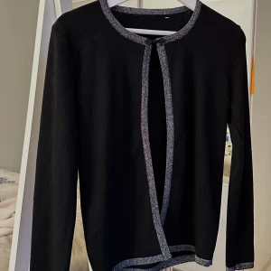 Kofta - En svart kofta med glitter detalj. Ett knäppe längs upp till. Passar perfekt att ha över en top eller klänning.
