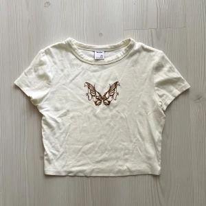 Croppad t-shirt med fjäril - Bershka - En söt, äggvit och kort t-shirt topp med fjärilstryck och tight fit! Bara använd två-tre gånger, så superfresh i kvalité! Legat i garderoben sedan dess och väntat på en ny ägare! Storlek M men sitter som något mellan S och M. 