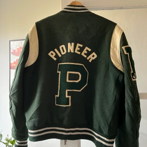 Collage jacka pioner  - En jätte snygg mörkgrön collage jacka med beiga detaljer samt både rygg och arm detaljer. Perfekt för både vår sommar och höst. inga skador förutom lite slitage på insidan men detta syns inte när man har på den och man märker inte av det alls. Skriv för fler bilder eller funderingar:)