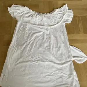 En vit Svea klänning. Den är off-shoulders och har ärmar under volangen. Den har även två fickor (en på vardera sida). Den är aldrig använd. Den är en S men passar även fint på M