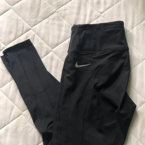 Träningstights Nike - Svarta högmidjade träningstights från Nike i storlek S. Tightsen är stretchiga, bekväma och hög i midjan (Squatproof). Baktill finns en liten ficka med dragkedja och på sidan av vänstra benet finns en till liten ficka. Tightsen är varsamt använda (fåtal gånger) och säljs då det inte kommer till användning, pågrund av att jag har andra tights. Köparen står för frakten, men pris kan diskuteras. Kontakta mig vid frågor och för mer information🤍