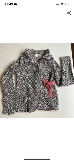 Omlottkofta S - Underbar omlottkofta i storlek S. Använd men i fint begagnat skick! Inte nopprig men hade en lös tråd vid höger ärm. (Bild 1) Den har jag nu fäst in så det syns inte. Rosa stickade band för knytning både fram och bak. Två små fickor framtill.