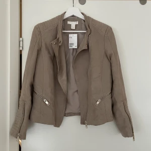 Mockajacka bikermodell - En beige jacka i mockaimitation strl 36. Bikermodell med fina detaljer. Aldrig använd, lappen kvar. 🤎