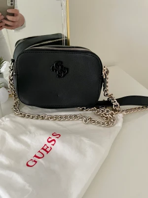 Guess väska  - Guess damväska , svart med lång kedja i silver (ej justerbar). Endast använd 1 gång. Kommer med dustbag. 