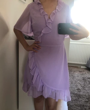 Lila omlottsklänning med volanger - Lila klänning i omlottsmodell med volanger. Storlek: XS Märke: Glamourus  Inte använd, nyskick. 