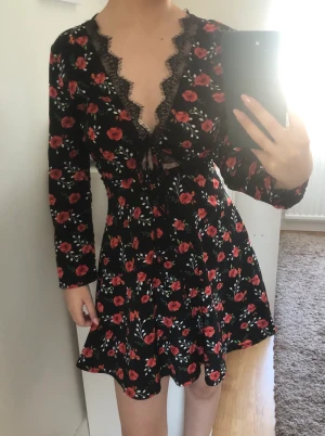 Svart blomming klänning  - Svart klänning med blommönster, spets och knytning framtill.  Storlek: 34 Märke: Missguided  Använd 1 gång, nyskick 