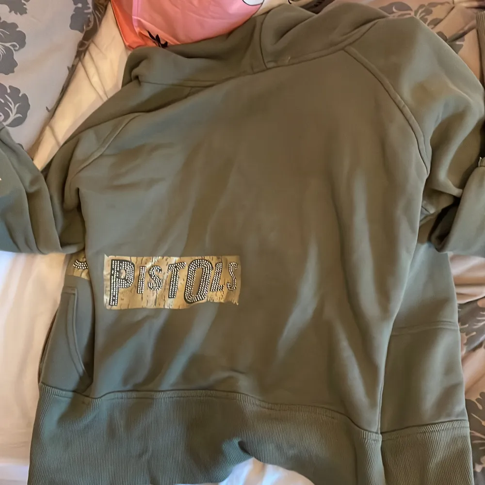 Super fin militär grön hoodie med med rhinestone tryck där det står  Sue’s (framme) pistol (bakom) och jewel på armen. Köpte den på second hand butik lokalt. Hittade ingen användning så jag säljer här på Plick!   Köparen står för frakt!. Hoodies.