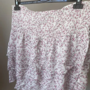 Blommig kjol - Kort, blommig kjol med volanger samt resår upptill. Aldrig använd.   Köparen står för frakten!