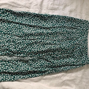 Grön blommig lång kjol  - Det är en grön kjol med vita blommor, den har en slits för benet och sedan knappar. Jag säljer den för att den är för liten. Den har även exktraknappar.  Inget fel 