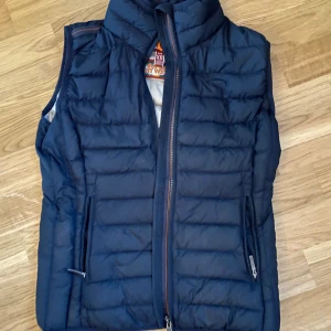 Parajumper väst st XS - Hej! Säljer min parajumper väst som jag fick hem idag då den är för liten över bysten för mig. Den är mörk marinblå men jag hade blixt på bilderna därför ser den så blå ut. Den är äkta😊