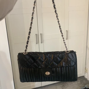 Väska - Svarta praktiskt väska där man kan ha den på föera sätt då kedjan är rörlig. Den är ungefär 25x15x3 cm och rymmer en del. Nyskick