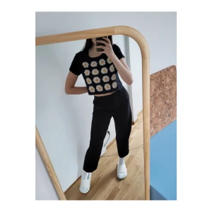 Blommig croppad T-shirt - Svart bomulls-T-shirt med prästkragar. Croppad design. Använd men i mycket fint skick (inga skador). Storlek: S men passar XS.