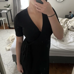 Svart omlottklänning - Jätte fin svart omlottklänning! Där klänningen går ihop är den fastsydd så den åker inte upp om man kan oroa sig för det! Använd en gång, med andra ord väldigt bra skick. Lite större i storleken så passar helt klart en S. 