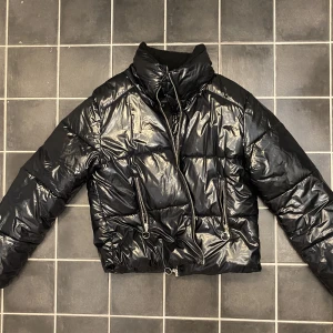 Svart puffer jacka - Snygg glansig puffer Jack det stå L i jackan men skulle säga S. Den e snyggt glansig o bra skicka fina detaljer på de fungerande dragkedjorna! Jackan är lite kroppade och snygg när man har lågmidgqt. Fin både öppen o stängd.
