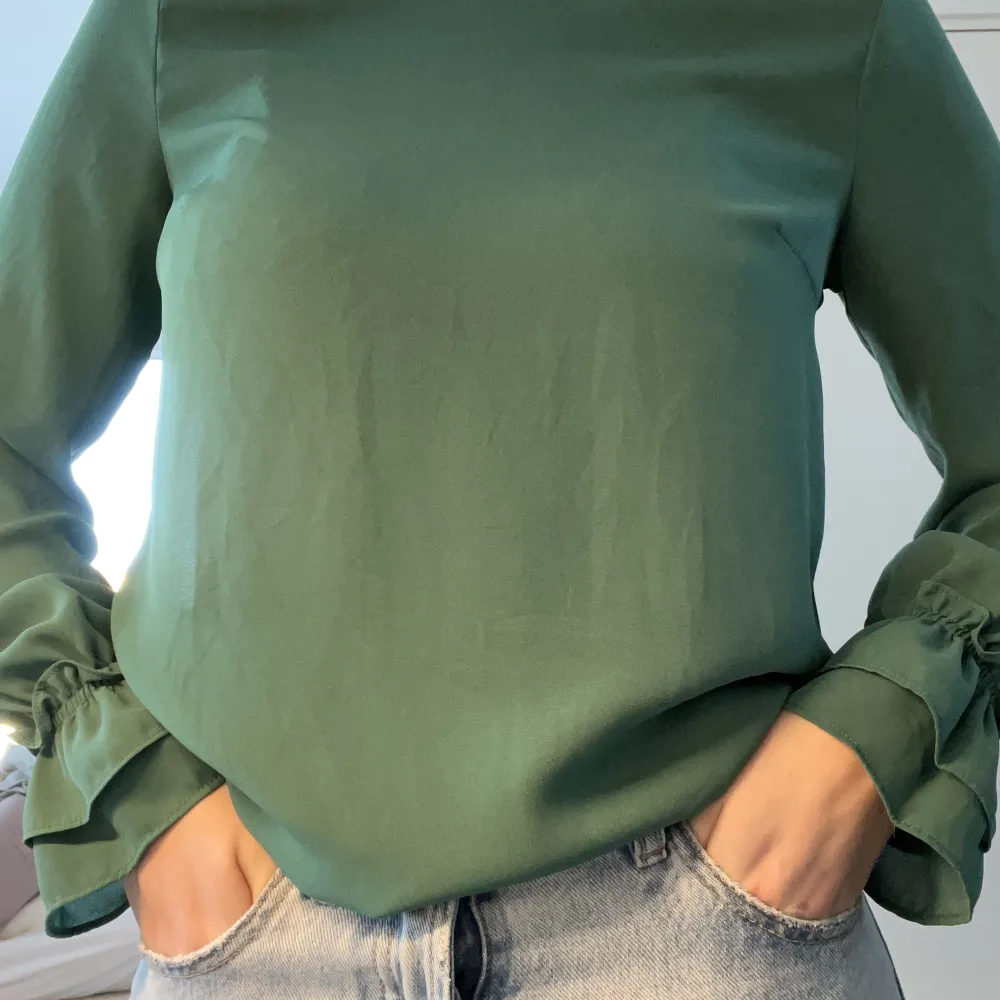 Grön blus från Gina Tricot med volang i armslutet. Även väldigt fint att ha under en stickad tröja. Blusen är i storlek 34, men passar även 36 och är i fint skick. Blusar.