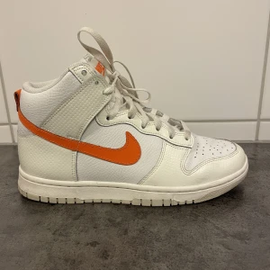 Nike Dunk High White/Orange - Nike Dunk High i vitt med orange swoosh. Modell DV6986-100.   Stl 39 med innermått 25cm enligt lapp.   Inköpa Nike Store 2022. De är använda ett fåtal ggr så i mkt fint skick. Tyvärr har sonen slängt kartongen. 