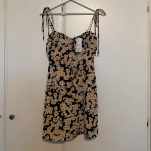 Ny blommig klänning - Ny med prislapp kvar. Dragkedja på sidan och justerbara axelband och justerbart band framtill. Passar bäst för XXS/XS