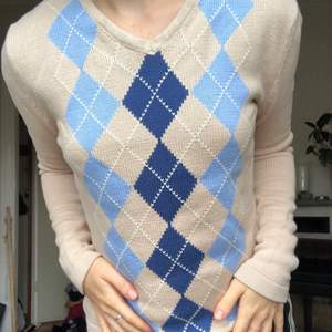 En stickad tröja med rutigt mönster i (inte alls stickigt) bomullsmaterial. Beige med blåa förger.