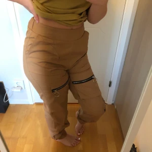 Beige cargo byxor - Beige byxor med dragkedjor från Boohoo, storlek 36, har lappen kvar så aldrig använda förutom när foton till annonsen togs!