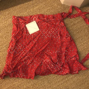 Wrap mini kjol (miniskirt) - Aldrig använd. Röd med vitblåa detaljer. Kort. Wrap skirt. Märke ”house of sienna”, tror dock jag beställde den från princess polly. Storlek 10 Amerikansk storlek!