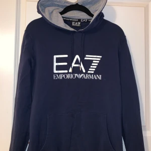 Armani hoodie dam - Mörkblå hoodie från Emporio Armani med grått tyg inuti luvan, loggan på bröstet är i silver. Tröjan är i storlek M men passar även S och XS. Den är i mycket bra skick, precis som ny då den bara har använts ett fåtal gånger. Nypris: 1099 kr.