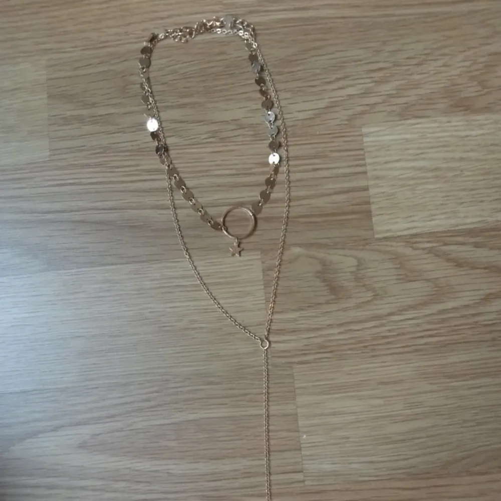 Halsband i guldfärgad metall i 2 lager med en stjärna och en stav i andra änden. Övrigt.