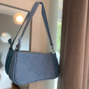 Ljusblå väska med krokodilmönster - Ljusblå väska med krokodilmönster. Endast använd en gång därav nyskick. Insidan är vinröd med ett fack.