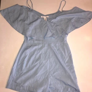 En playsuit från NLY TREND - En ljusblå playsuit som endast är använd 1 gång. Storlek 36. Finns en liten dragkedja på ena sidan. Från Nelly. 100% polyester.