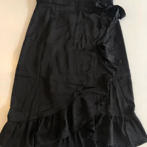 Neo Noir midikjol omlott - Neo Noir omlottkjol i midi-modell. Svart. Storlek S/36 men genom att den knyts själv fungerar den även för större och mindre storlekar. Använd endast en gång. 