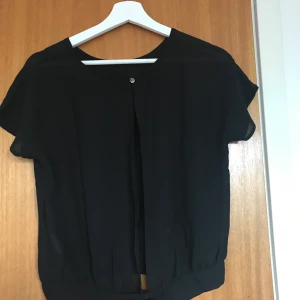 Svart blus med öppen rygg och knytning  - En jätte fin blus som passar till precis allt! Blusen har en snygg knytning längst ned med öppen rygg. Storleken är xs och skicket är väldigt bra  