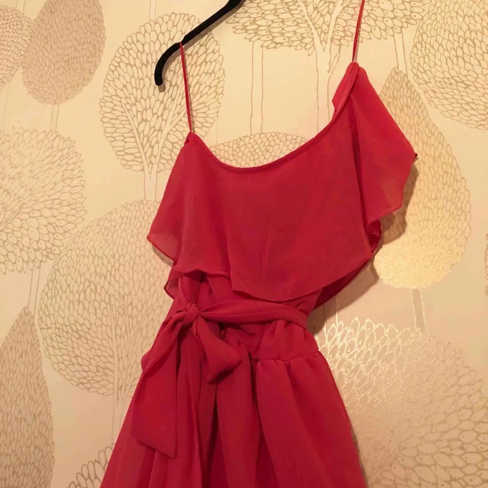 Rosa klänning som går ungefär till knäna Ena axeln är bar och klänningen knyts med snöre i midjan. Klänningar.
